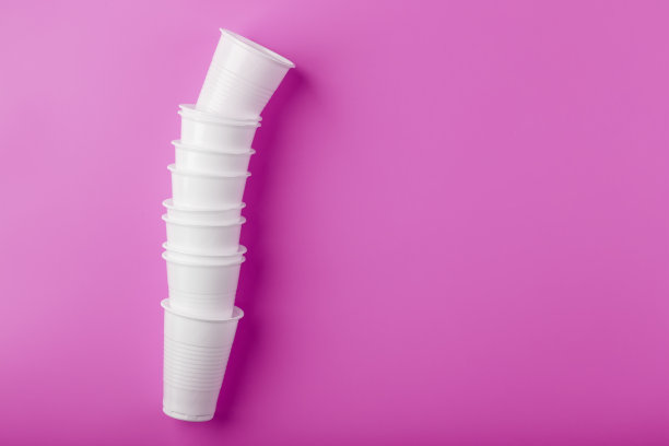 一排一次性白色塑料餐具眼镜，粉红色背景。图片下载