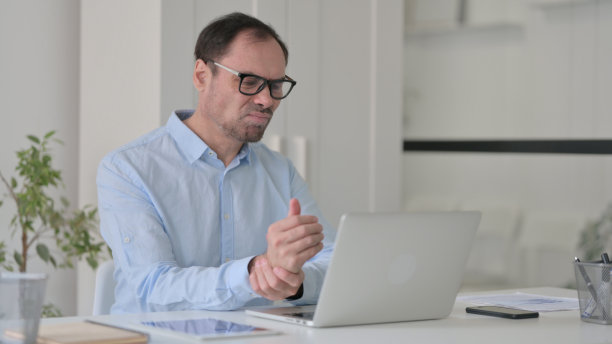 中年男子在使用笔记本电脑时手腕疼痛图片下载