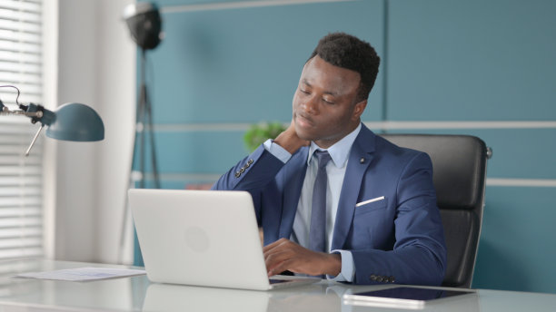 非洲商人在办公室使用笔记本电脑时颈部疼痛图片下载