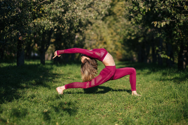 一名身着红色运动服的年轻女子在秋天的公园里摆出瑜伽战士的姿势。图片下载