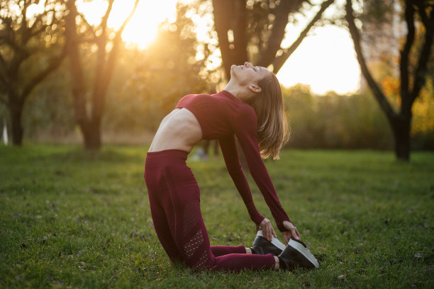 在秋天的公园里，一名身着红色运动服的年轻女子在夕阳下做瑜伽。图片下载