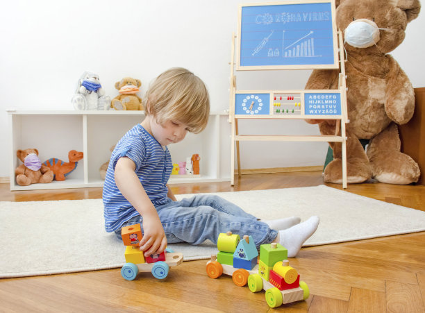在冠状病毒大流行封锁期间，可爱的男孩在家里的地板上玩木制玩具，并在黑板上画出了COVID-2019病例的增长图表图片下载