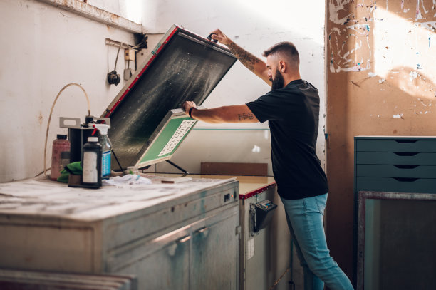 男性工人在印刷车间工作时使用丝网曝光装置图片下载