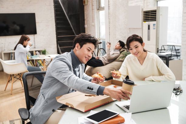 年轻的生意人一边工作一边吃披萨图片下载