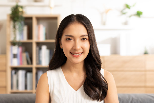 快乐美丽的亚洲女人的肖像看着相机微笑与积极的情绪。聪明自信的自由职业女性微笑快乐的在家工作或学习年轻女性视频电话在线学习。素材图片