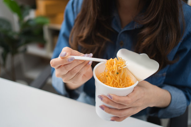 商务女性在工作场所吃辣面坐在办公室，桌上放着笔记本电脑，不健康的生活方式吃快餐的概念。图片下载