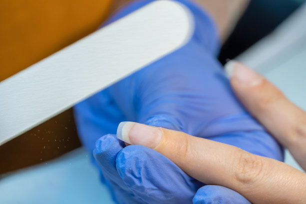 一个在蓝色手套美甲大师的特写锉指甲用一个特殊的指甲锉，宏。钉治疗过程图片下载