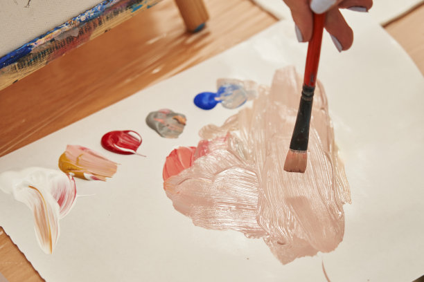 在一张纸上涂上几滴颜料，然后用一只女性的手把它们混合在一起图片下载