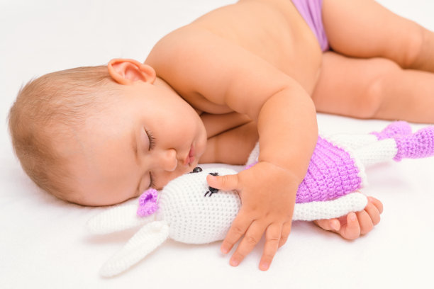 一个12-17个月大的漂亮新生儿抱着一个针织兔子玩具睡着了。图片下载