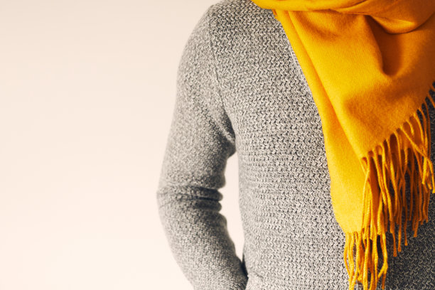 一个男人穿着开襟羊毛衫，围着黄色围巾，背景很淡。副本的空间。图片下载