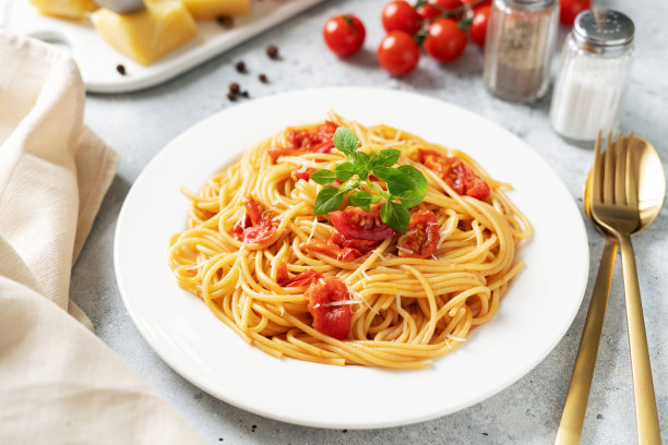 明亮的厨房桌子上白色盘子里的意大利面配番茄，帕尔马干酪和罗勒。传统意大利面，蔬菜和奶酪特写图片下载