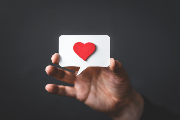 一个男人手里拿着一颗红色的心，在黑色的背景上说话。复制的空间。积极反馈和反馈。图片下载