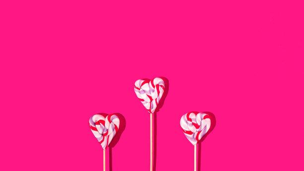 鲜艳的洋红色背景上的三颗彩色心形棒棒糖。情人节卡片或横幅或婚礼邀请的创意概念。母亲节广告艺术设计。图片下载