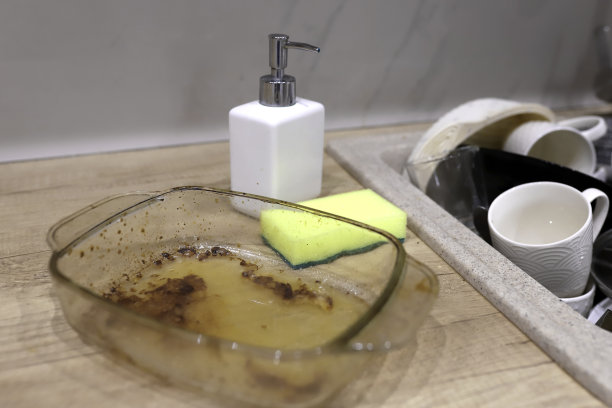 烤肉用的脏兮兮的长方形旁边放着一堆脏盘子。用耐热玻璃制成的空托盘，烤盘旁边放着海绵和洗碗精图片下载