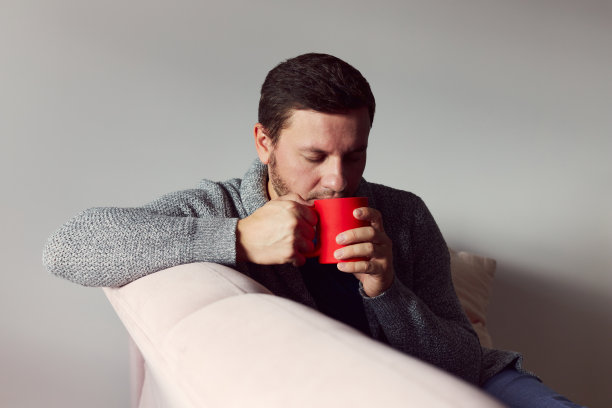 一个男人手里拿着一杯红色的咖啡，穿着一件开襟羊毛衫。秋天的概念。图片下载