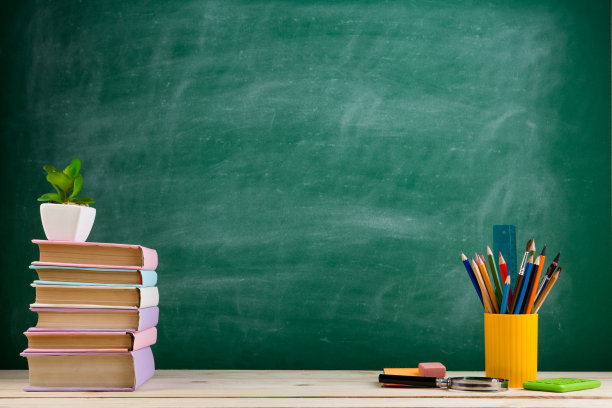教育与阅读概念——教室里的木桌上摆放着一组五颜六色的书籍，背景是黑板图片下载