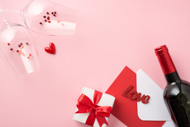 俯视图照片的情人节装饰心脏葡萄酒杯五彩纸屑白色礼盒红色蝴蝶结信封红色卡片题词爱和酒瓶在单独的淡粉色背景与空白空间图片下载