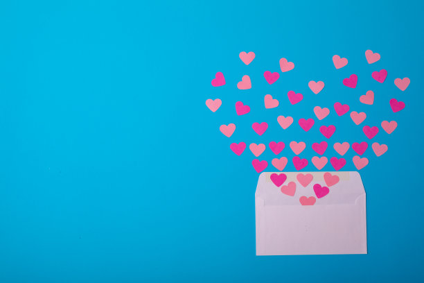 从蓝色背景的白色信封上出来的粉红色心的俯视图，复制空间图片下载