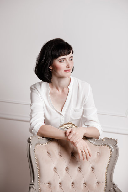 画室里有一张迷人的年轻女子的肖像，她一头黑发，穿着白衬衫和红裤子，斜靠在一张经典的椅子上，背景是纯白色的。专横的女性，面试理念，自信独立的女性图片下载