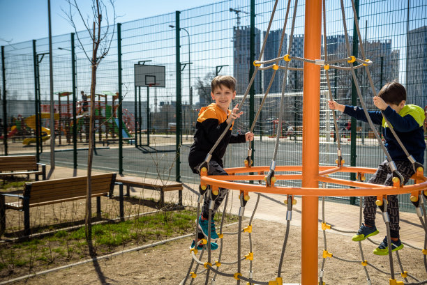 两个小男孩活跃的小男孩在弹簧金属游乐场玩爬山，他的手在户外锻炼。温暖的阳光明媚的日子。友谊的概念图片下载