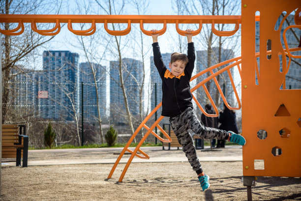 一个可爱的男孩正在操场上攀爬。他有一张非常开心的脸，喜欢独自在户外冒险运动。温暖的阳光明媚的日子图片下载