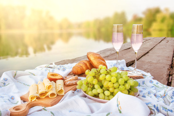 在河边的木桥上进行浪漫的野餐，有香槟、水果、糕点和奶酪。放松图片下载