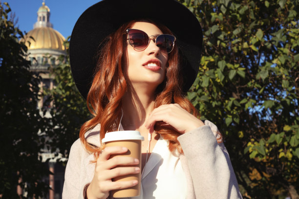 微笑时尚的年轻女子喝咖啡，走在城市的街道上图片下载