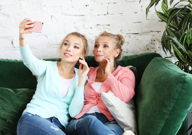美丽成熟的母亲和她的女儿用智能手机和微笑自拍图片下载