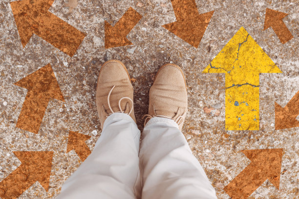 一个穿着靴子的人站在灰色的柏油路上，黄色的箭头指向方向。图片下载