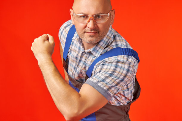 戴着防护眼镜，穿着工作服的秃头男子，展示着他的力量图片下载