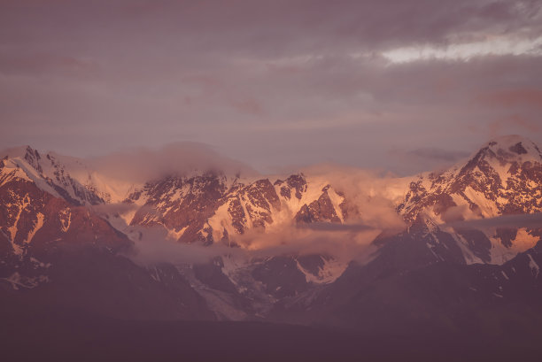 风景优美的山地景观，巨大的雪山山脉被黎明的太阳照射在低云之间。令人敬畏的高山风景，在日落或日出时高高的山脊。大冰川在顶部，复古的颜色图片下载