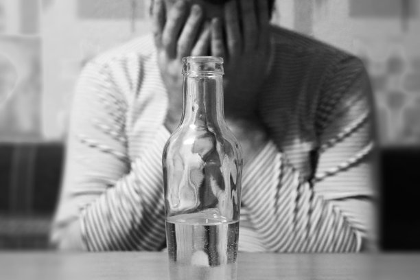 一个男人在厨房的桌子旁，还有一瓶伏特加。宿醉的头痛。一个男人抱着他的头。单色图像。背景。图片下载