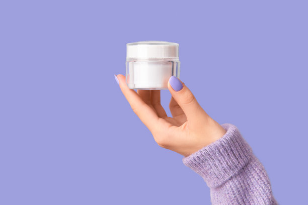 女人的手在紫罗兰色的背景上拿着白色的管。皮肤保健理念。图片下载