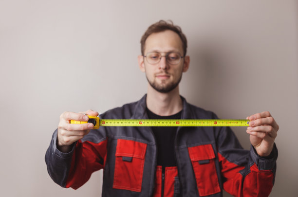 房子装修的概念。无法辨认的修理工拿着卷尺在蓝色背景下，特写镜头。全景图片下载