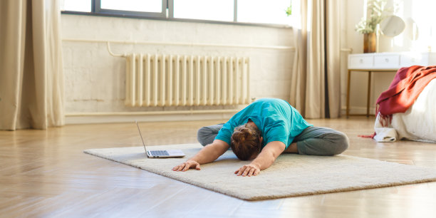 瑜伽和普拉提练习——一名年轻男子在室内的笔记本电脑前伸展身体。格式照片2 x1图片下载