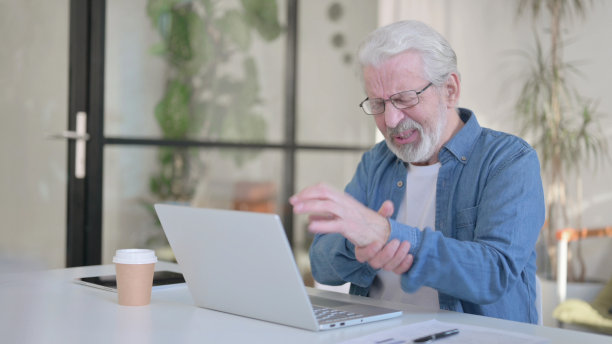 老人在办公室使用笔记本电脑时手腕疼痛图片下载