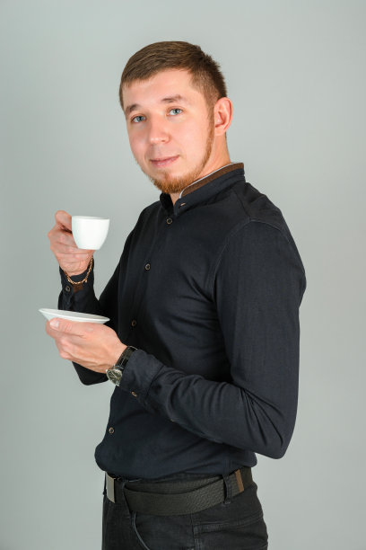 一个留着胡子的红头发的年轻男子看着镜头，用一个白色的小杯子喝着咖啡图片下载