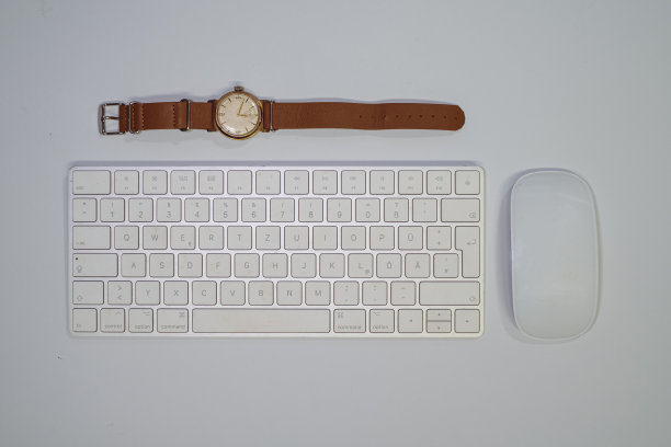 一块旧手表放在一个白色键盘和一个白色鼠标旁边图片下载