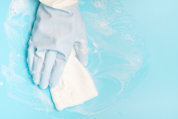 女性手用橡胶手套用抹布擦拭表面，蓝色背景图片下载