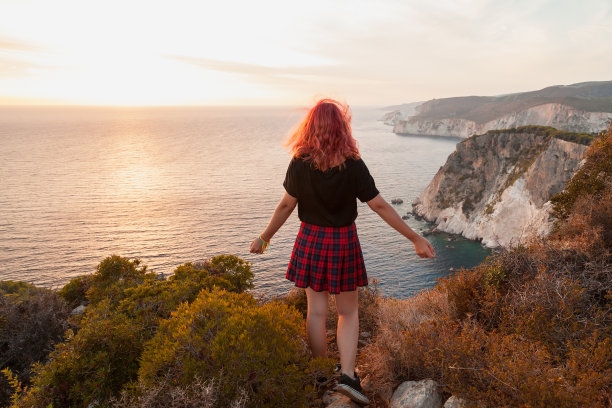 一个穿着红色裙子的少女站在海边的悬崖上图片下载