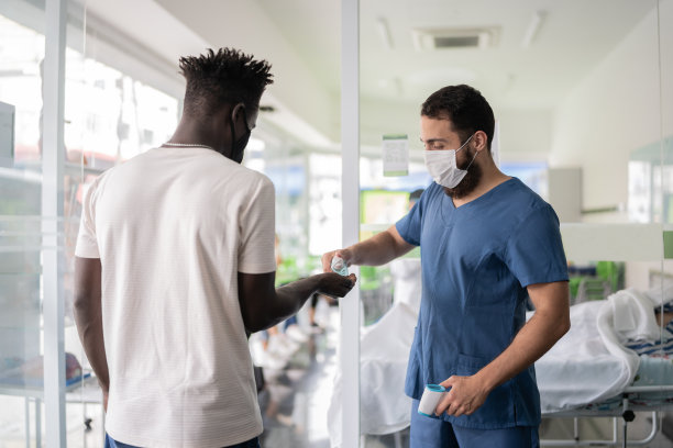 护士为排队等候进入疫苗接种中心的年轻人测体温并提供洗手液图片下载