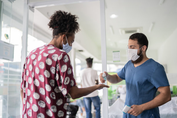 护士为排队等候进入疫苗接种中心的年轻人测体温并提供洗手液图片下载