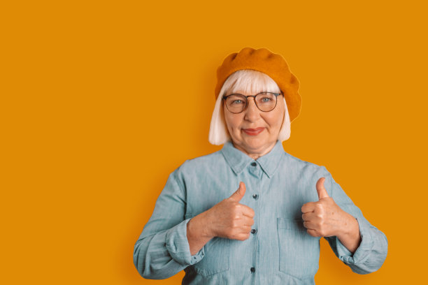 在明亮的橙色背景下，50多岁的白人女性在工作室里竖起大拇指，表现出良好的情绪图片下载