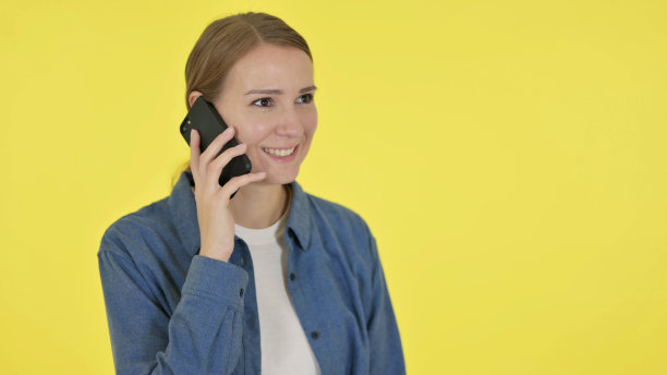 年轻女子在黄色背景下讲电话图片下载