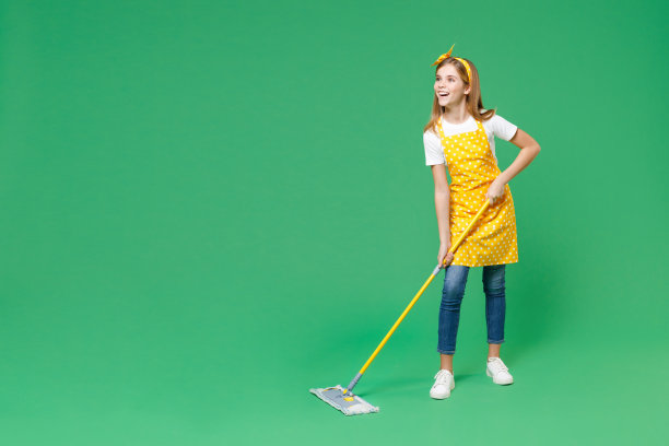 满脸笑容的小女孩，家庭主妇12-13岁，穿着黄色围裙，用拖把洗地板，一边做家务，一边在绿色背景的儿童画室肖像。管家的概念。图片下载
