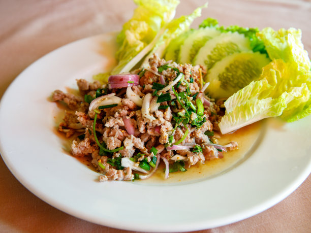 泰国菜，用勺子和叉子在白色盘子上放上辛辣的猪肉末沙拉图片下载