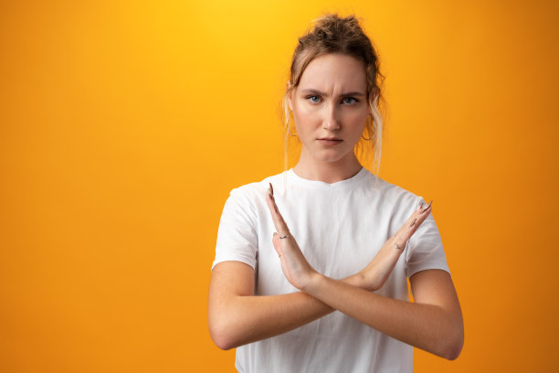 年轻少女交叉双臂，在黄色背景下做着消极的手势图片下载