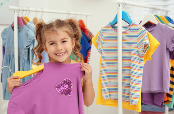 小女孩在室内的衣架上挑选衣服图片下载