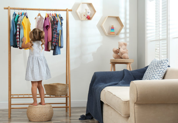 小女孩在客厅的衣架上挑选衣服图片下载