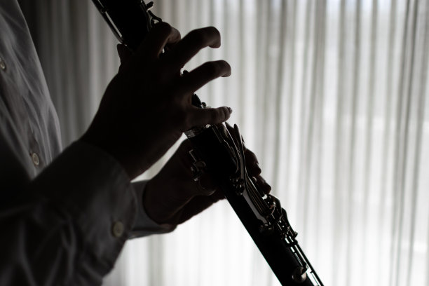 年轻美丽的女士，享受在她的家里演奏她的单簧管，在窗口练习，享受她的音乐和自由时间。图片下载